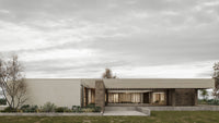 Modern house with a flat roof and large windows, set against a cloudy sky.