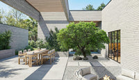 Modern outdoor patio area with a dining table, chairs, and a tree in a residential setting.